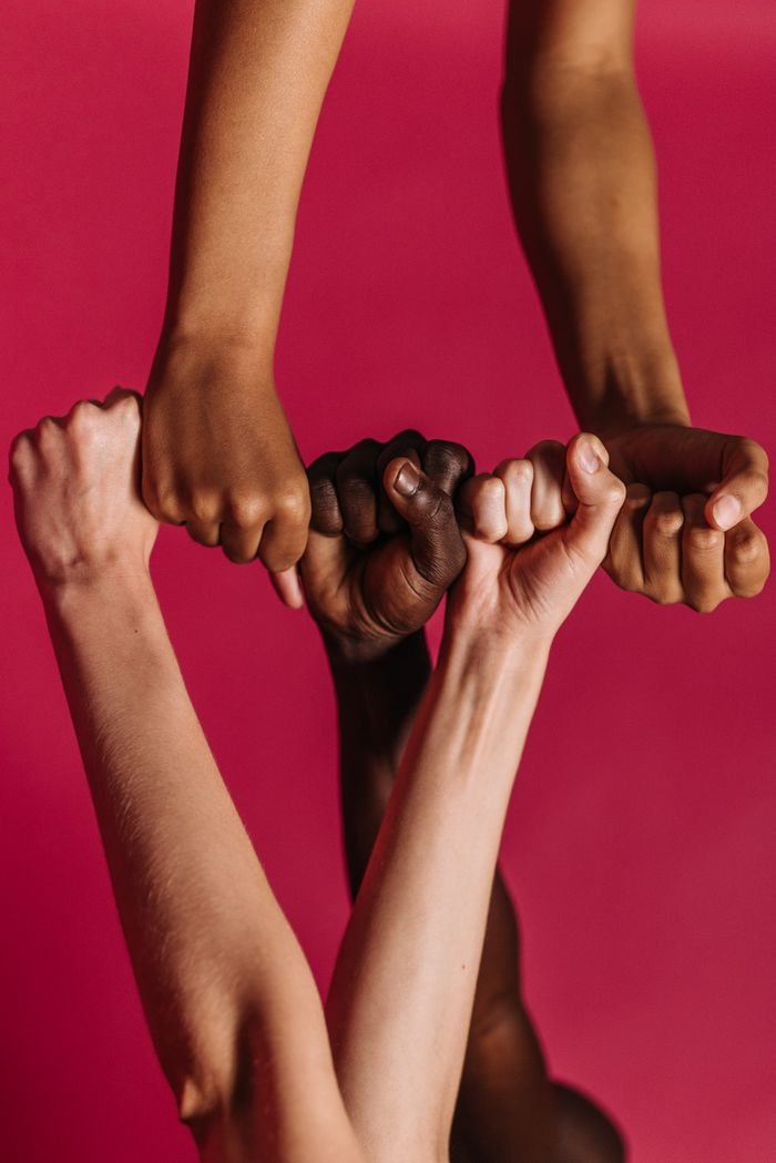 Four diverse arms join together in solidarity against a vibrant red backdrop.